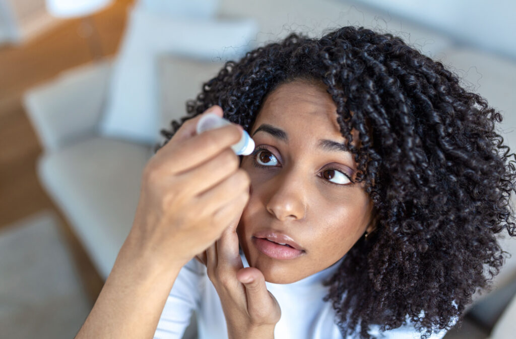 A young woman with curly hair pulling down her right lower eyelid to apply artificial tears on her right eye.