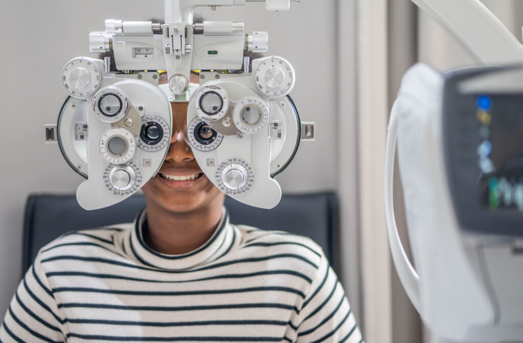 A person in a striped shirt looking through a phoropter as a part of an eye exam.