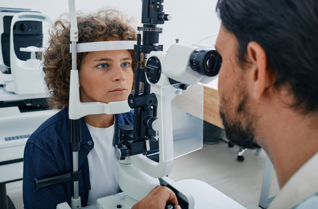 A boy with curly hair undergoing an eye exam while he rests his chin on a medical equipment.