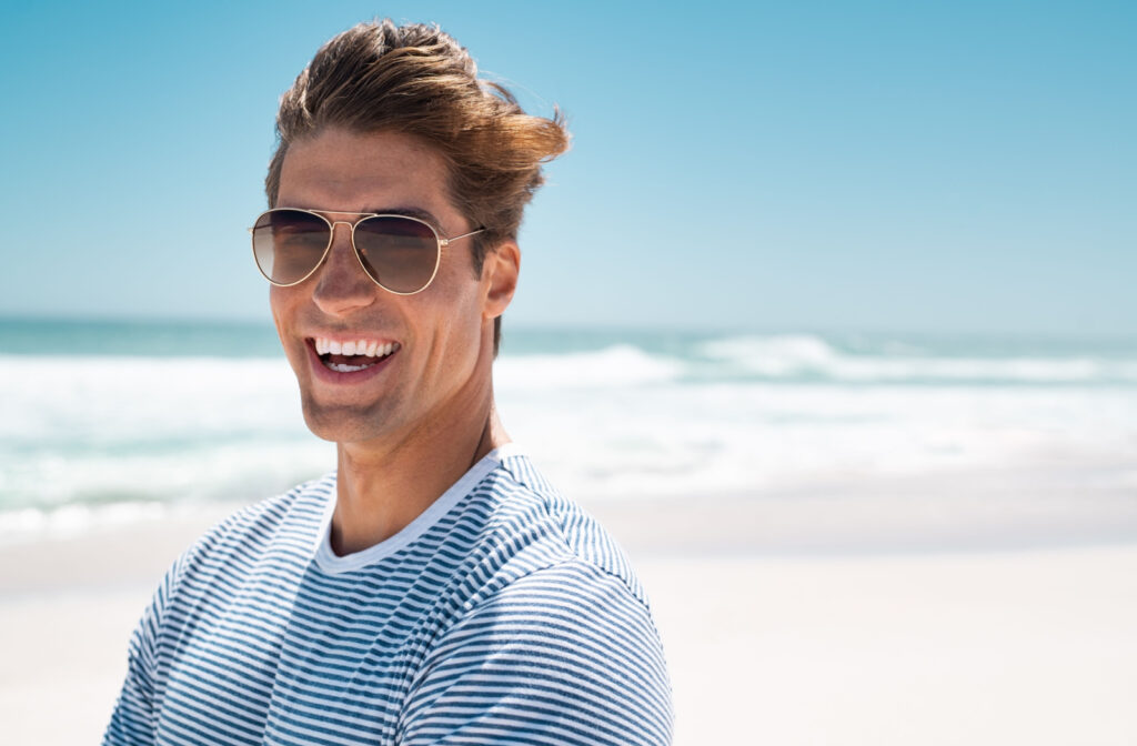 A young man by the beach wearing sunglasses to protect his eyes from the sun.