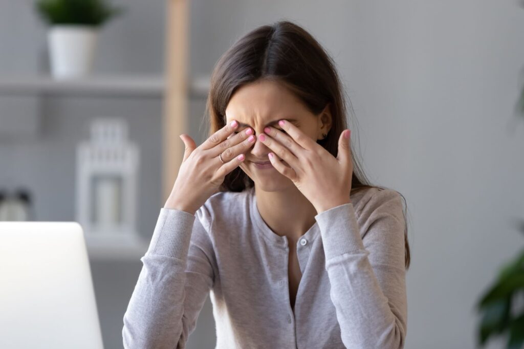 A woman is rubbing her eyes vigorously from unexplained eye pressure building in her eyes.