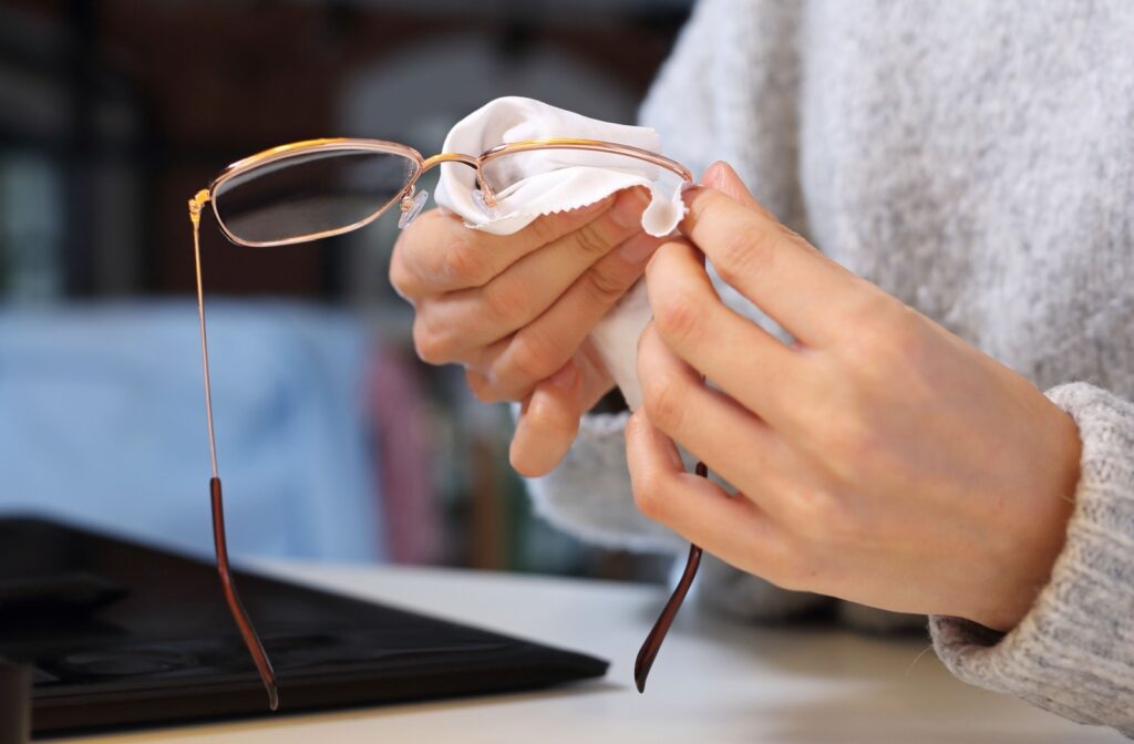 A woman cleaning her glasses with a cloth. She is holding the glasses in her left hand and using her right hand to wipe them clean with a small cloth.