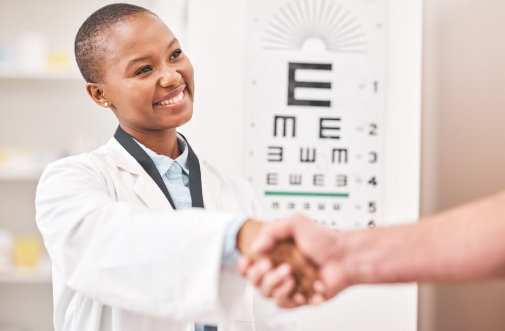 A young female optometrist smiling and shaking hands with a customer who is off camera.