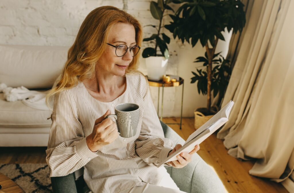 A person with progressive lenses sitting and reading a book while drinking coffee.