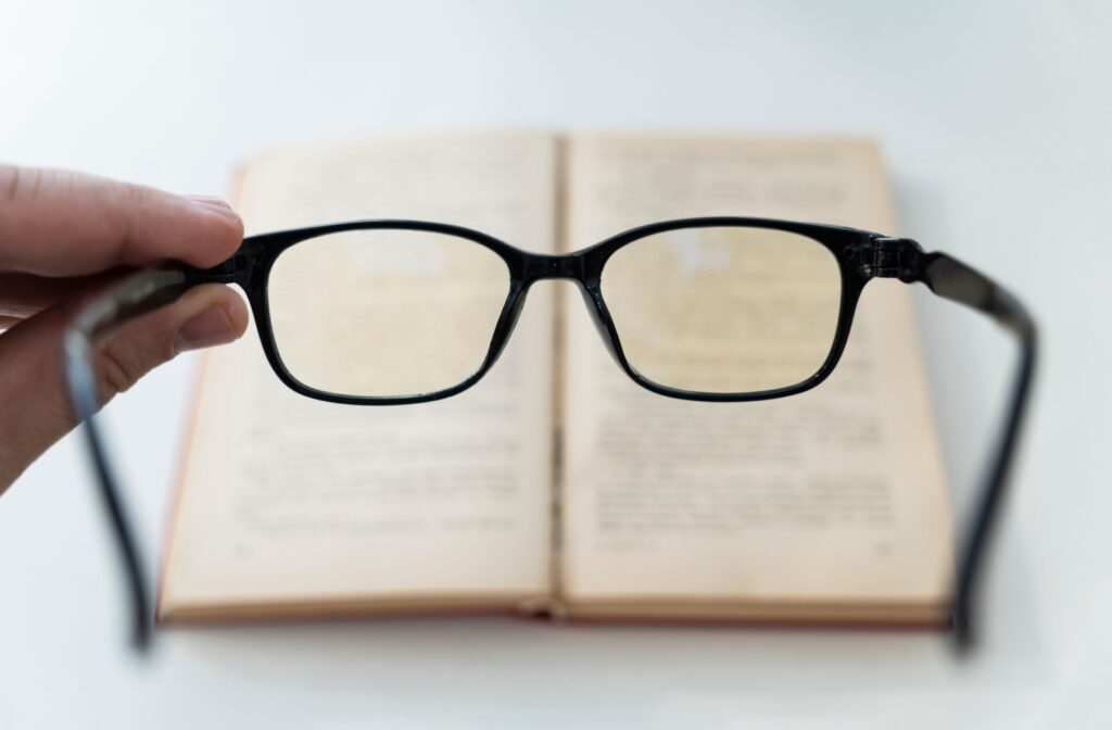 A first-person view of a pair of glasses held in front of a book correcting the blurry vision caused by myopia.